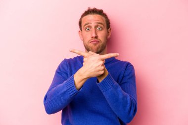 Pembe arka plan noktalarında izole edilmiş genç beyaz adam iki seçenek arasında seçim yapmaya çalışıyor..