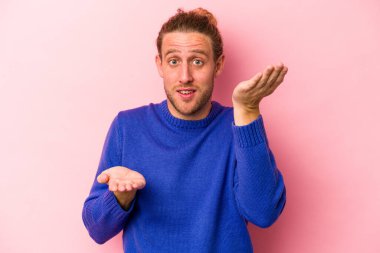 Pembe arka planda izole edilmiş genç beyaz adam kollarıyla ölçek oluşturuyor, mutlu ve kendinden emin hissediyor..