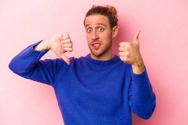 Pembe arka planda izole edilmiş genç beyaz bir adam baş parmağını kaldırıyor ve baş parmağıyla işaret ediyor. Zor bir seçim.