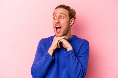 Pembe arka planda izole edilmiş genç beyaz adam ellerini çenesinin altında tutuyor, mutlu bir şekilde yana bakıyor..