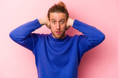 Kafkasyalı genç adam pembe arka planda izole edilmiş kulakları kulaklarıyla kapatıyor çok fazla ses duymamaya çalışıyor..