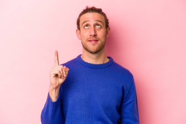 Pembe arka planda izole edilmiş genç beyaz adam iki parmağı da boş bir alan gösteriyor..