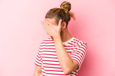 Pembe arka planda izole edilmiş genç beyaz adam elleriyle gözlerini kapatmaktan korkuyor..