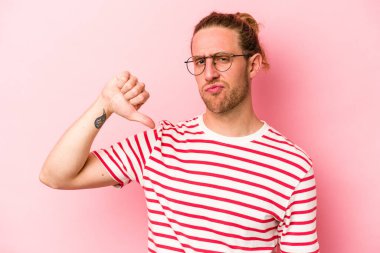 Pembe arka planda izole edilmiş genç beyaz adam baş parmağını aşağı gösteriyor, hayal kırıklığı konsepti..