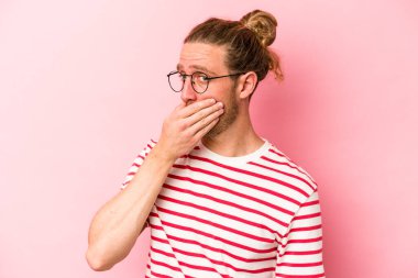 Pembe arka planda izole edilmiş genç beyaz adam elleri endişeli bir şekilde ağzı örtüyor..