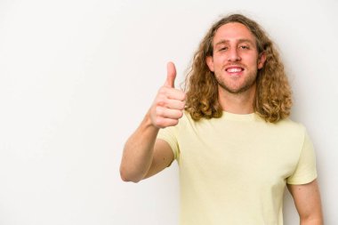 Beyaz arka planda izole edilmiş genç beyaz adam gülümsüyor ve başparmağını kaldırıyor.