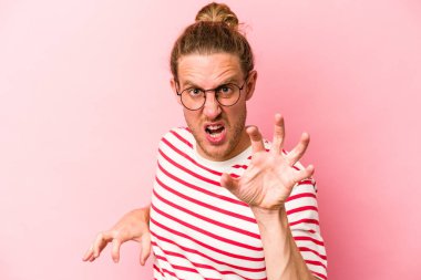 Pembe arka planda izole edilmiş genç beyaz adam pençelerini kedi taklidi yaparken gösteriyor, agresif bir hareket..