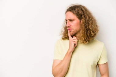 Beyaz arka planda izole edilmiş genç beyaz bir adam şüpheli ve şüpheci bir ifadeyle yana bakıyor..