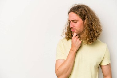 Beyaz arka planda izole edilmiş genç beyaz bir adam şüpheli ve şüpheci bir ifadeyle yana bakıyor..