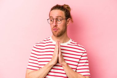 Genç beyaz adam pembe arka planda izole edilmiş dua ediyor, bağlılık gösteriyor, dindar biri ilahi ilham arıyor..