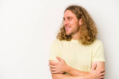 Beyaz arka planda izole edilmiş genç beyaz adam kollarını kavuşturarak gülümsüyor..