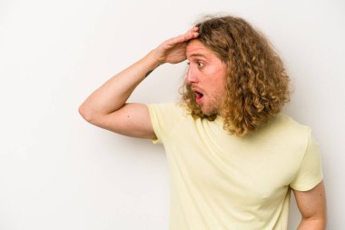 Beyaz arka planda izole edilmiş genç beyaz bir adam uzaklara bakıyor ve elini alnına koyuyor..