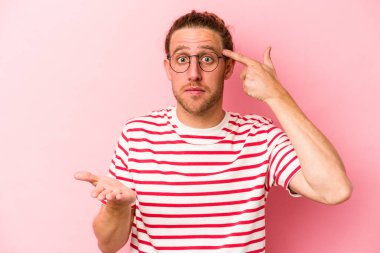 Pembe arka planda izole edilmiş genç beyaz adam elinde bir ürün tutuyor..