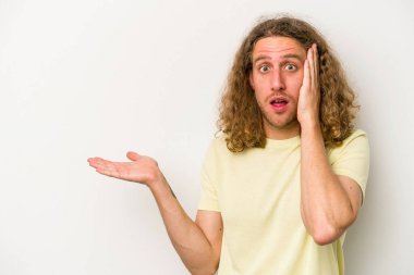 Beyaz arka planda izole edilmiş genç beyaz adam, avuç içi fotokopi alanını elinde tutmaktan etkilenmiş..