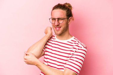 Genç beyaz adam pembe arka planda izole edilmiş dirsek masajı yapıyor, kötü bir hareketin ardından acı çekiyor..