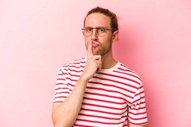 Kafkasyalı genç adam pembe arka planda izole edilmiş düşünüyor ve yukarı bakıyor, yansıtıyor, düşünüyor, bir fantezi kuruyor..