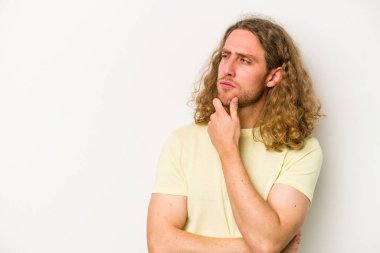 Beyaz arka planda izole edilmiş genç beyaz bir adam rahatlamış bir şeyin fotokopi odasına baktığını düşünüyor..