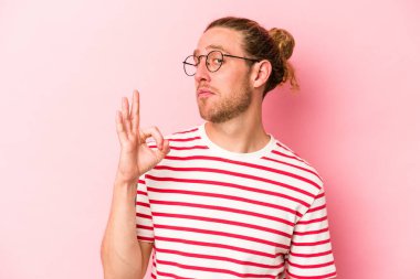 Pembe arka planda izole edilmiş genç beyaz bir adam bir göz kırptı ve elleriyle iyi bir jest yaptı..
