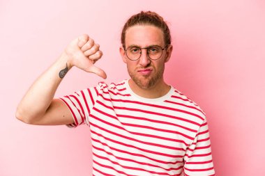 Pembe arka planda izole edilmiş genç beyaz adam baş parmağını aşağı gösteriyor ve hoşlanmadığını ifade ediyor..