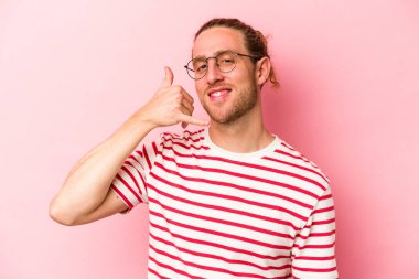 Pembe arka planda izole edilmiş genç beyaz adam parmaklarıyla bir cep telefonu hareketi gösteriyor..