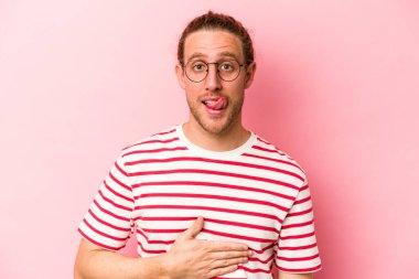 Pembe arka planda izole edilmiş genç beyaz adam karnına dokunuyor, nazikçe gülümsüyor, yemek yiyor ve tatmin oluyor..