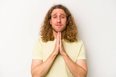 Beyaz arka planda izole edilmiş genç beyaz bir adam el ele tutuşup, ağız kenarında dua ediyor, kendinden emin..