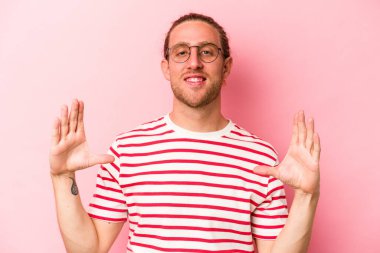 Pembe arka planda izole edilmiş genç beyaz bir adam elinde avuç içi bir şeyle kameraya sunuyor..