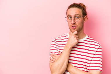 Pembe arka planda izole edilmiş genç beyaz adam şüpheli ve şüpheci bir ifadeyle yana bakıyor..