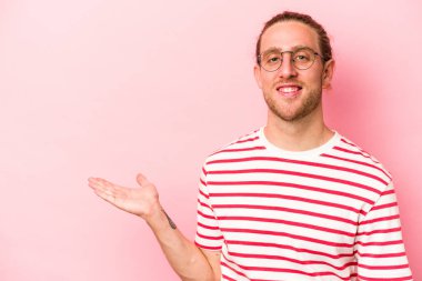 Pembe arka planda izole edilmiş genç beyaz bir adam bir palmiye üzerinde fotokopi alanı ve belinde başka bir el tutuyor..