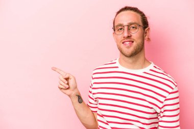Pembe arka planda izole edilmiş genç beyaz adam işaret parmağıyla işaret ederek gülümsüyor..