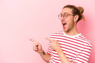 Kafkasyalı genç adam pembe arka planda izole edilmiş, başparmak uzakta, gülüyor ve kaygısız..