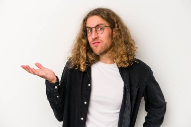 Beyaz arka planda izole edilmiş genç beyaz bir adam sorgulama sırasında omuz silkiyor ve şüphe duyuyor..