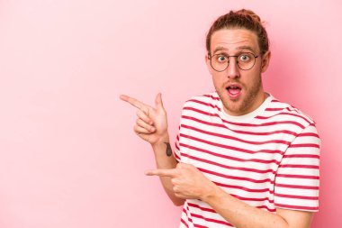 Pembe arka planda izole edilmiş genç beyaz adam işaret parmağıyla işaret ederek heyecanlanıyor..
