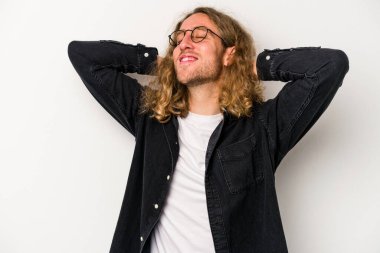 Beyaz arka planda izole olmuş genç beyaz bir adam kendini güvende hissediyor, elleri başının arkasında..