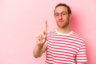 Pembe arka planda izole edilmiş genç beyaz bir adam bir numarayı parmağıyla gösteriyor..