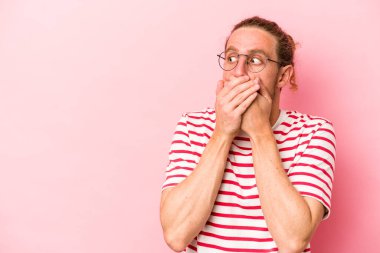 Pembe arka planda izole edilmiş genç beyaz bir adam. Düşünceli bir şekilde ağzıyla ağzını kapatan bir fotokopi odasına bakıyor..