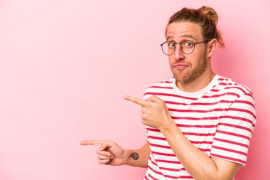 Pembe arka planda izole edilmiş genç beyaz adam işaret parmağıyla fotokopi alanını işaret ederek şok oldu..