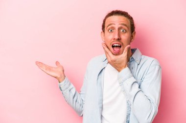 Pembe arka planda izole edilmiş genç beyaz bir adam avucunun içinde fotokopi alanı tutuyor, el üstünde tutuyor. Şaşırmış ve mutlu..