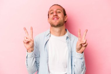 Pembe arka planda izole edilmiş genç beyaz adam zafer işareti gösteriyor ve gülümsüyor..