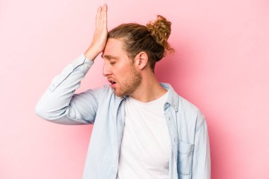 Pembe arka planda izole edilmiş genç beyaz bir adam bir şeyi unutuyor. Alnına avuç içi ve gözlerini kapatarak vuruyor..