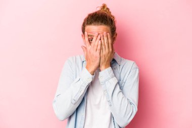 Pembe arka planda izole edilmiş genç beyaz adam kameraya parmaklarıyla göz kırpıyor, yüzünü kapatmaktan utanıyor..