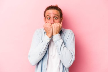 Pembe arka planda izole edilmiş, tırnak yiyen, gergin ve endişeli genç bir beyaz adam..