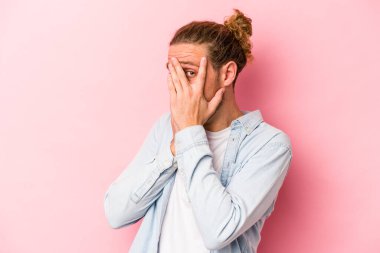 Pembe arka planda izole edilmiş genç beyaz adam parmaklarıyla gözünü kırp korkmuş ve gergin..