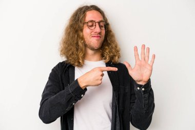 Beyaz arka planda izole edilmiş genç beyaz bir adam gülümseyerek beş numarayı parmaklarıyla gösteriyor..