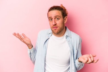 Pembe arka planda soyutlanmış genç beyaz bir adam sorgulama sırasında omuz silkiyor ve şüphe duyuyor..