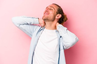 Pembe arka planda izole edilmiş genç beyaz bir adam kendini güvende hissediyor, elleri başının arkasında..