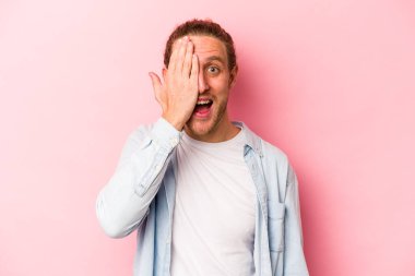 Pembe arka planda izole edilmiş genç beyaz adam yüzünün yarısını palmiye ile örterek eğleniyor..