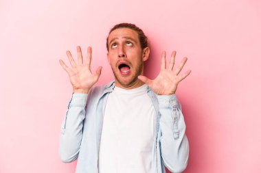 Pembe arka planda izole edilmiş genç beyaz adam gökyüzüne haykırıyor, yukarı bakıyor, hayal kırıklığına uğramış..