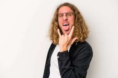 Beyaz arka planda izole edilmiş genç beyaz bir adam parmaklarıyla kaya hareketi gösteriyor.