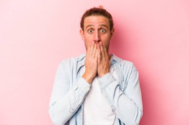 Pembe arka planda izole edilmiş genç beyaz adam elleriyle ağzını kapatırken şok oldu..